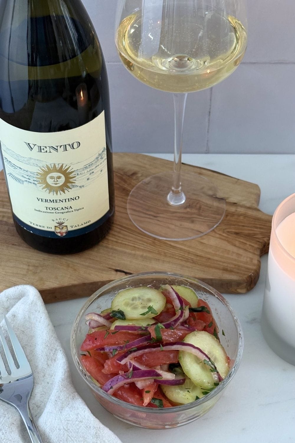 Bowl of tomato, cucumber, onion, and basil salad served beside a glass and bottle of Vermentino wine.