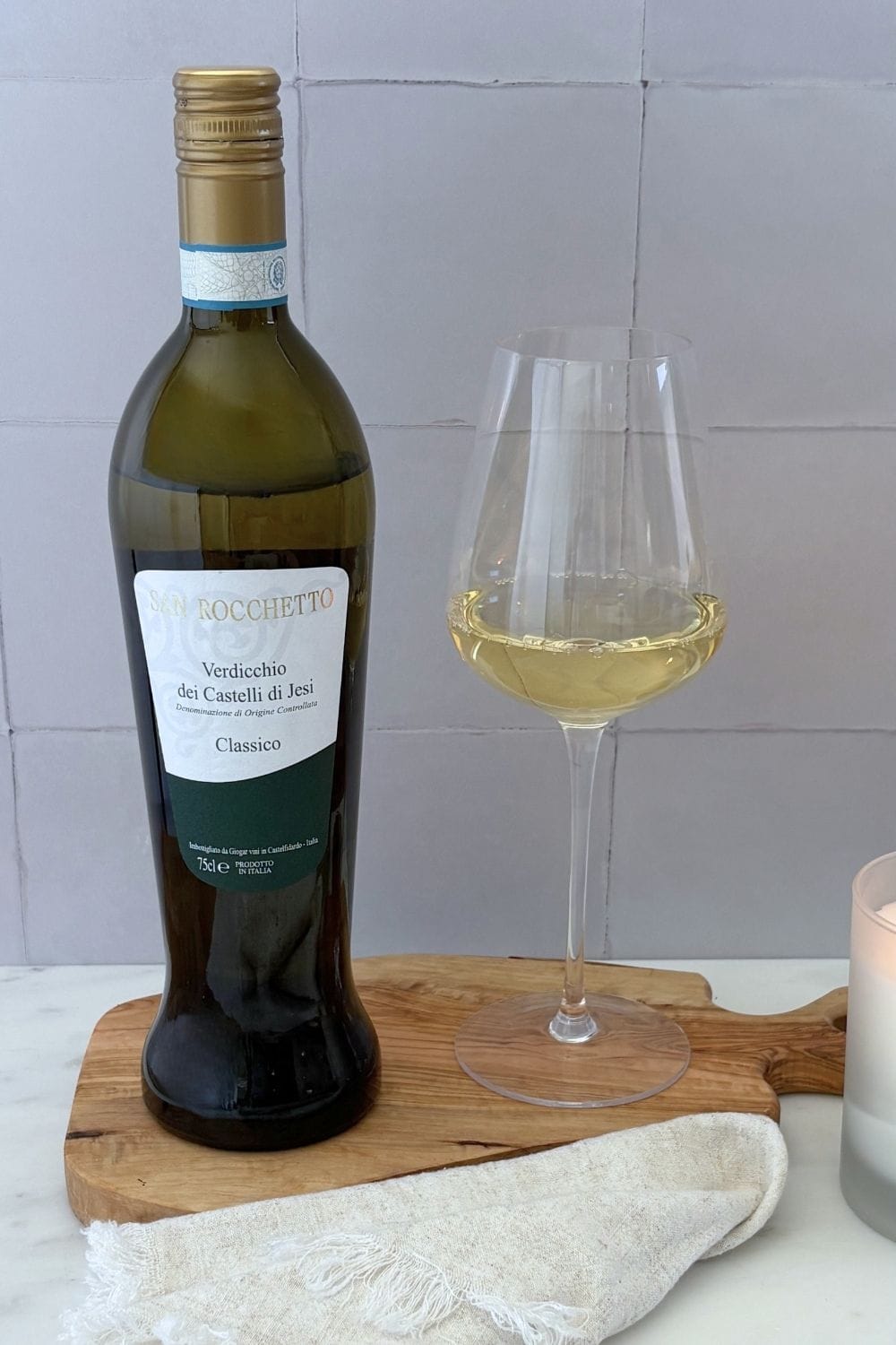 Bottle of Verdicchio dei Castelli di Jesi Classico with a glass of pale straw-colored white wine on an olive wood board.