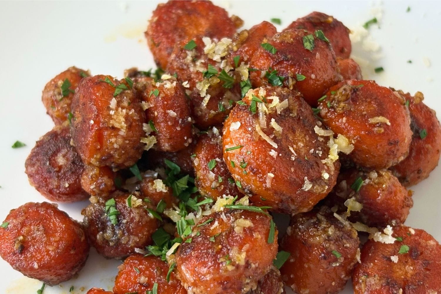 Close-up of braised carrots coated with Parmigiano-Reggiano, showing their browned edges, tender texture, and parsley garnish.