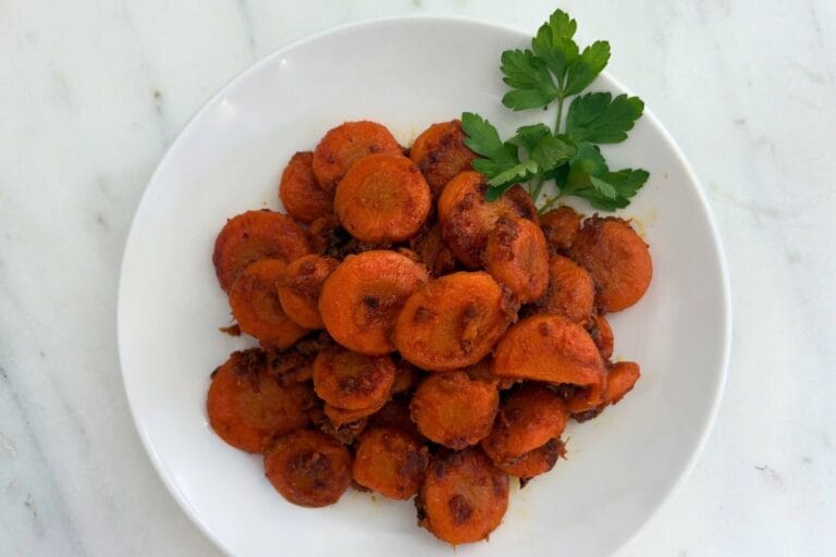 Overhead view of braised carrot slices with browned edges and Parmesan cheese, garnished with fresh parsley on a white plate.