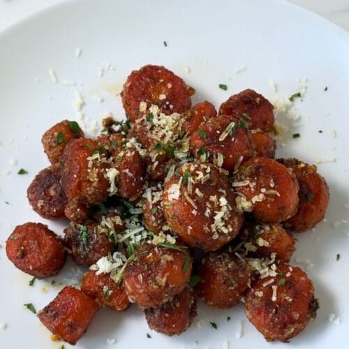 Marcella Hazan's Braised Carrots with Parmesan Cheese served in a white bowl, finished with freshly grated Parmigiano-Reggiano and chopped parsley.