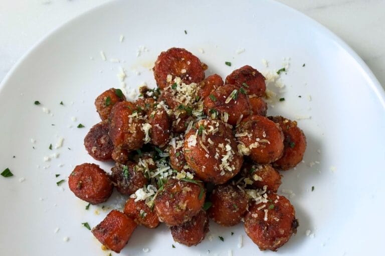 Marcella Hazan's Braised Carrots with Parmesan Cheese served in a white bowl, finished with freshly grated Parmigiano-Reggiano and chopped parsley.