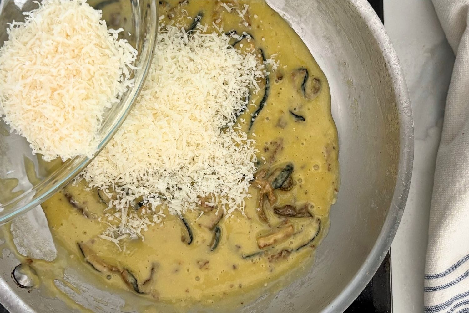 Freshly grated Parmigiano-Reggiano and Pecorino Romano being added to a creamy zucchini sauce with fried zucchini strips before tossing with fusilli pasta.