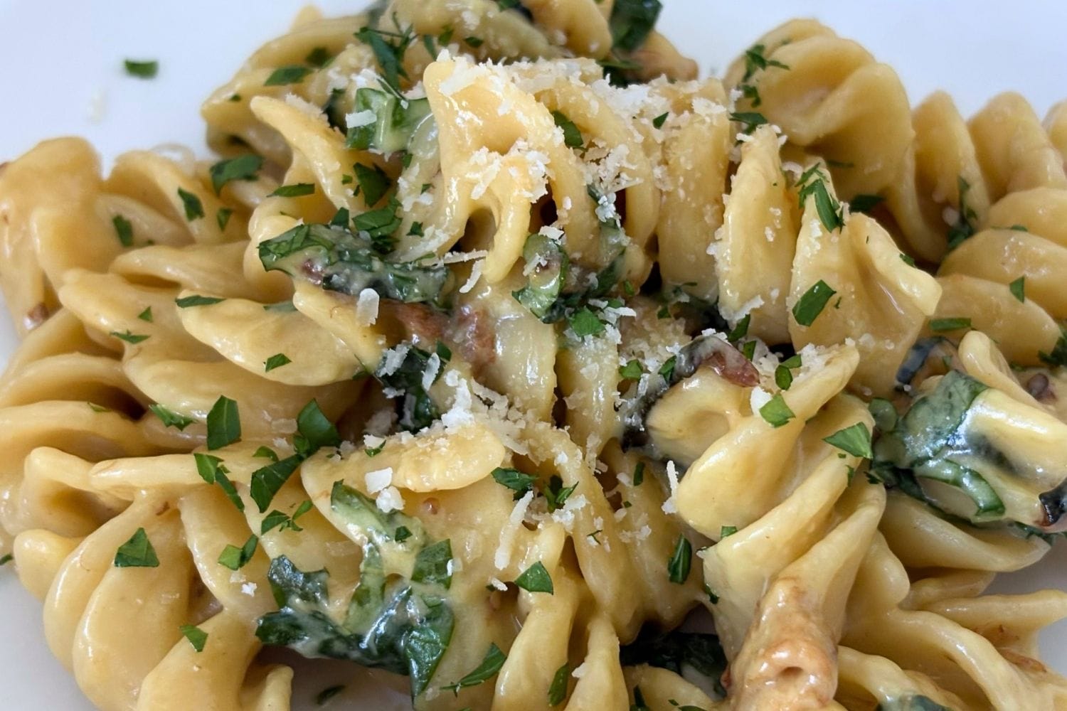 Close-up of fusilli pasta coated in a creamy zucchini and cheese sauce with fried zucchini strips, fresh basil, and grated Parmesan.
