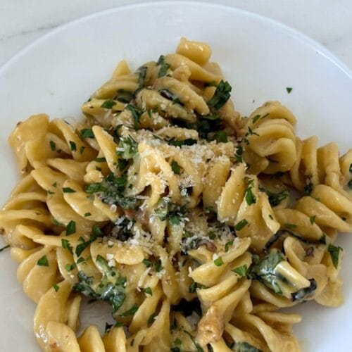 Plate of Marcella Hazan's fusilli with creamy zucchini and basil sauce topped with grated Parmesan and fresh basil, served with a glass of Soave wine.
