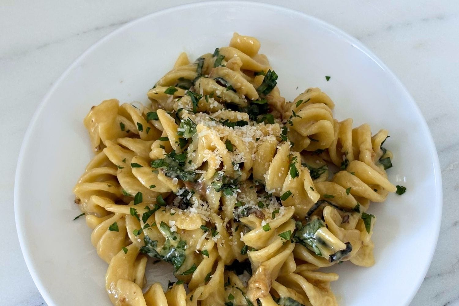 Plate of Marcella Hazan's fusilli with creamy zucchini and basil sauce topped with grated Parmesan and fresh basil, served with a glass of Soave wine.