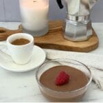 Glass bowl of Italian chocolate mousse garnished with a fresh raspberry served with a cup of espresso, a lit candle, and a stovetop moka pot.