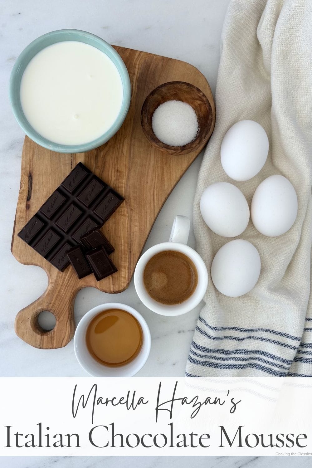 Ingredients for Marcella Hazan's Italian chocolate mousse including semisweet chocolate, eggs, heavy cream, espresso, dark rum, and sugar arranged on an olive wood board.