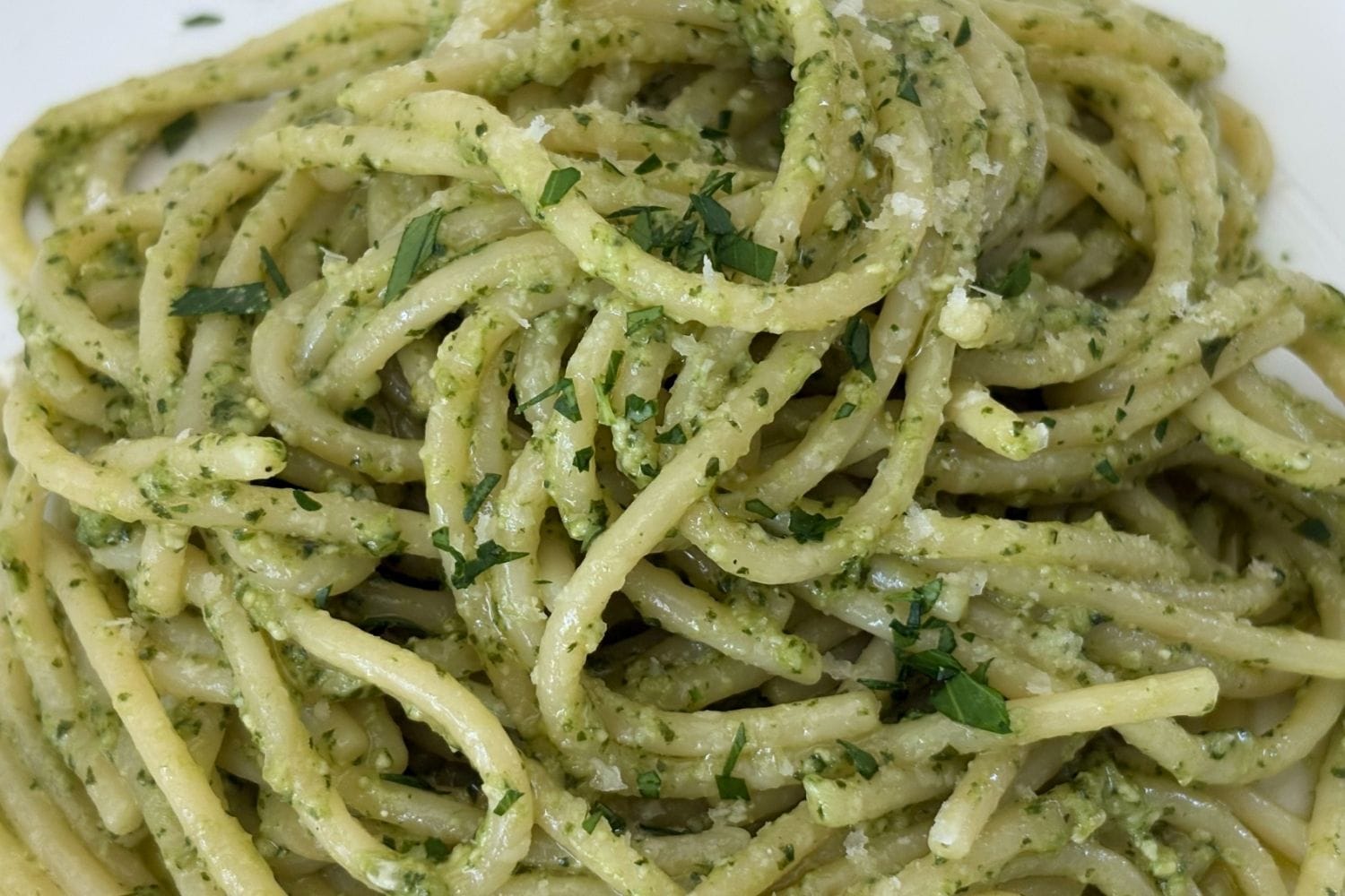 Close-up of spaghetti coated in creamy basil pesto with grated Parmigiano-Reggiano and chopped parsley.