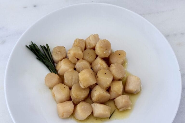 Sautéed scallops with rosemary and lemon served in a white bowl with olive oil sauce and fresh rosemary.