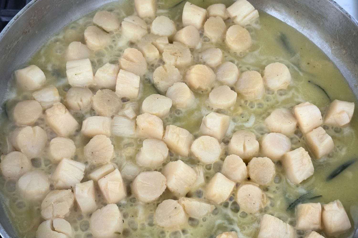 Scallops cooking in a skillet with olive oil, garlic, rosemary, and lemon sauce.