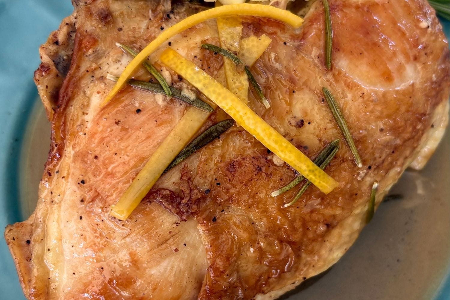 Close-up of Marcella Hazan's fricasseed chicken with rosemary and lemon, showing golden-brown chicken skin garnished with fresh rosemary and lemon zest.