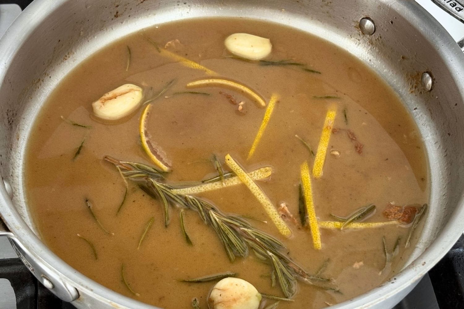 Pan sauce with white wine, garlic, rosemary, and lemon zest simmering after cooking chicken.