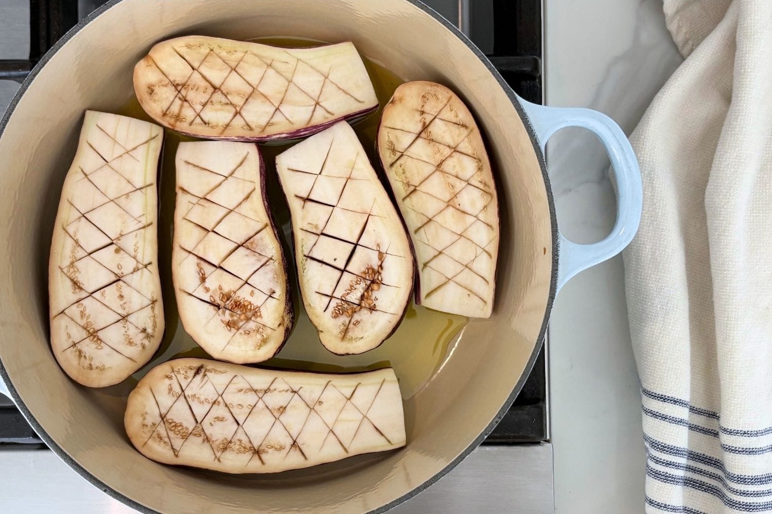Baby eggplant halves scored in a crosshatch pattern and sautéing cut-side down in olive oil in a Dutch oven.