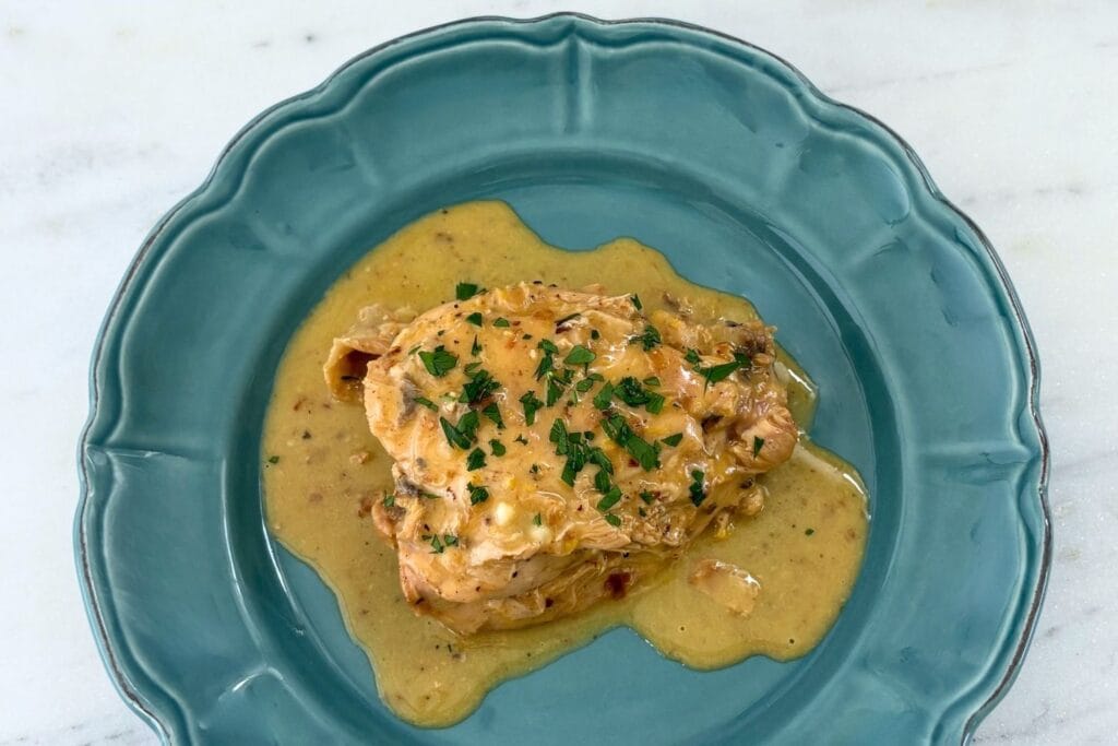 Fricasseed chicken with egg and lemon sauce served on a blue ceramic plate with chopped parsley.