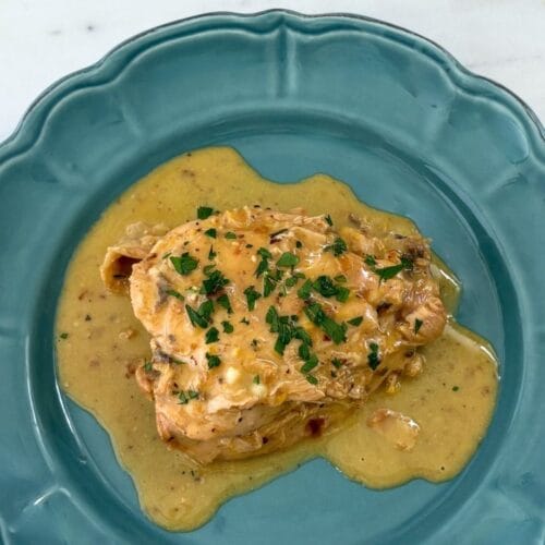 Fricasseed chicken with egg and lemon sauce served on a blue ceramic plate with chopped parsley.