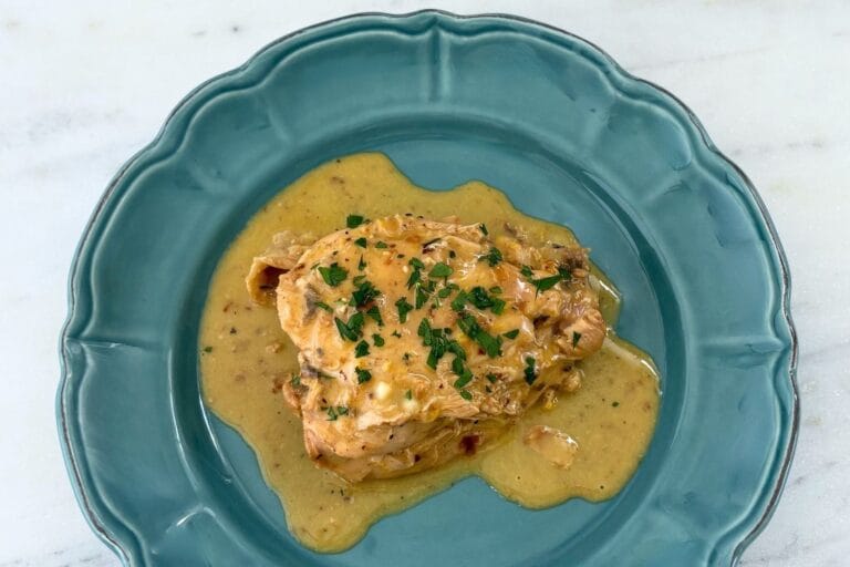 Fricasseed chicken with egg and lemon sauce served on a blue ceramic plate with chopped parsley.