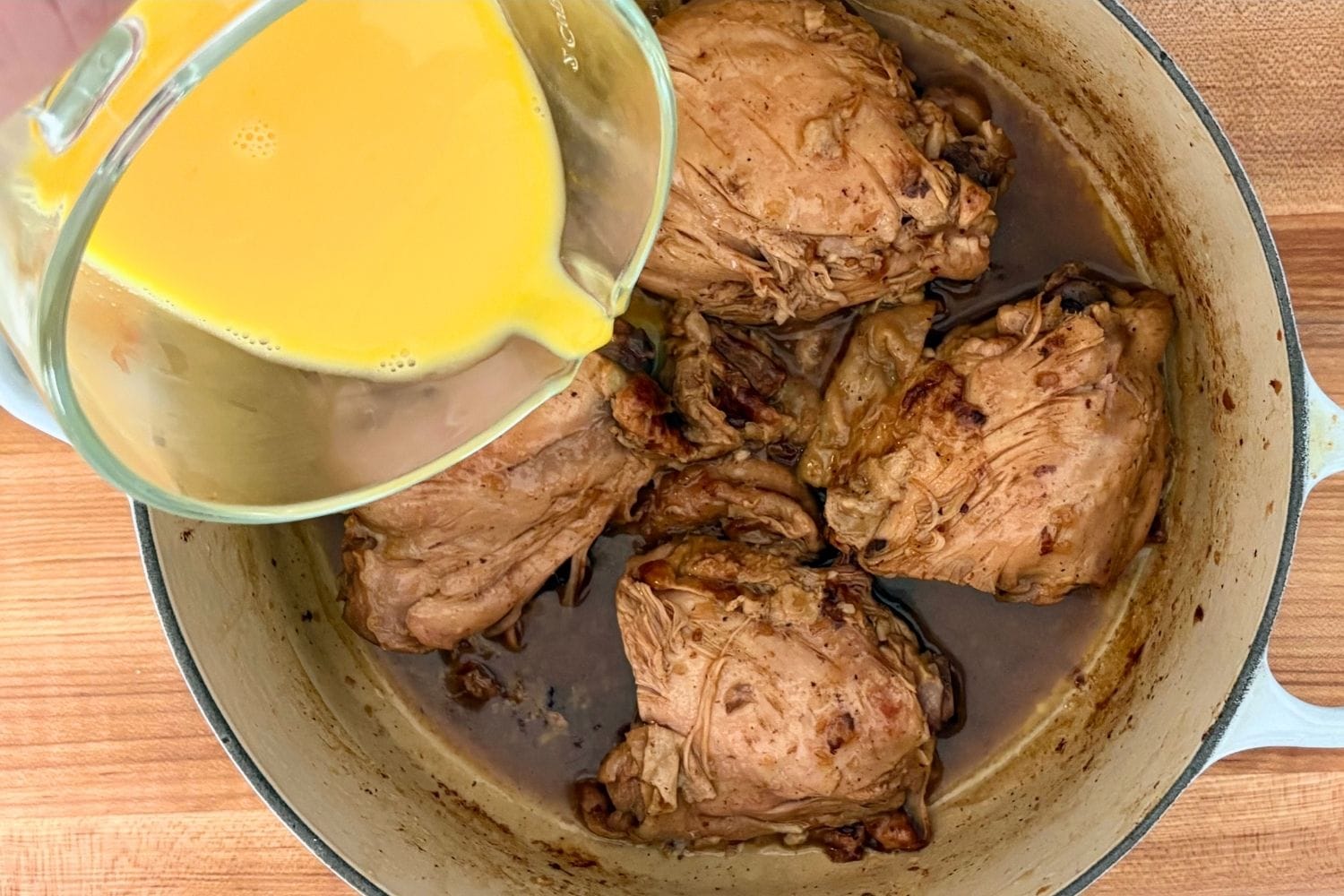 Beaten egg and lemon mixture being added to fricasseed chicken and cooking juices in a Dutch oven.