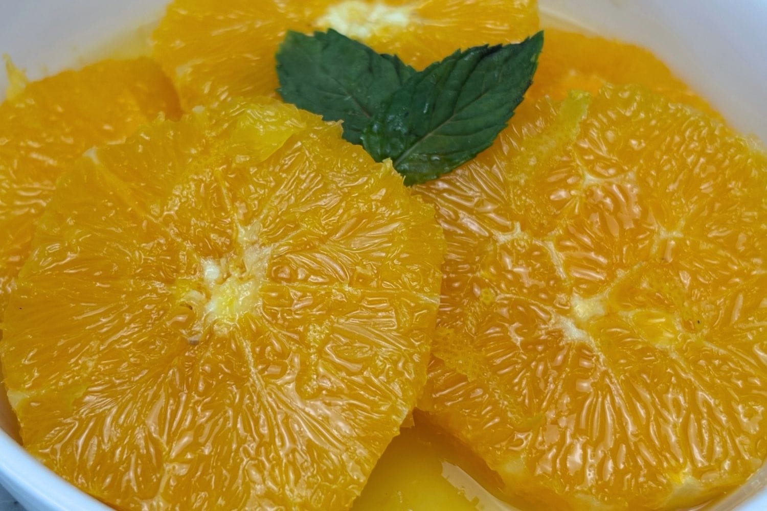 Close-up of juicy macerated orange slices with fresh mint and citrus juices.
