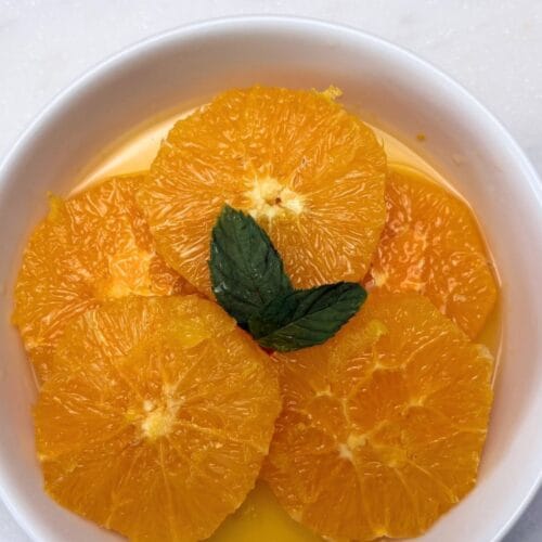 Macerated orange slices in their citrus juices, garnished with fresh mint in a white bowl.