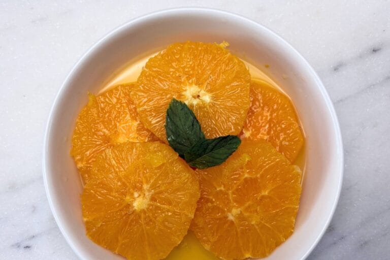 Macerated orange slices in their citrus juices, garnished with fresh mint in a white bowl.
