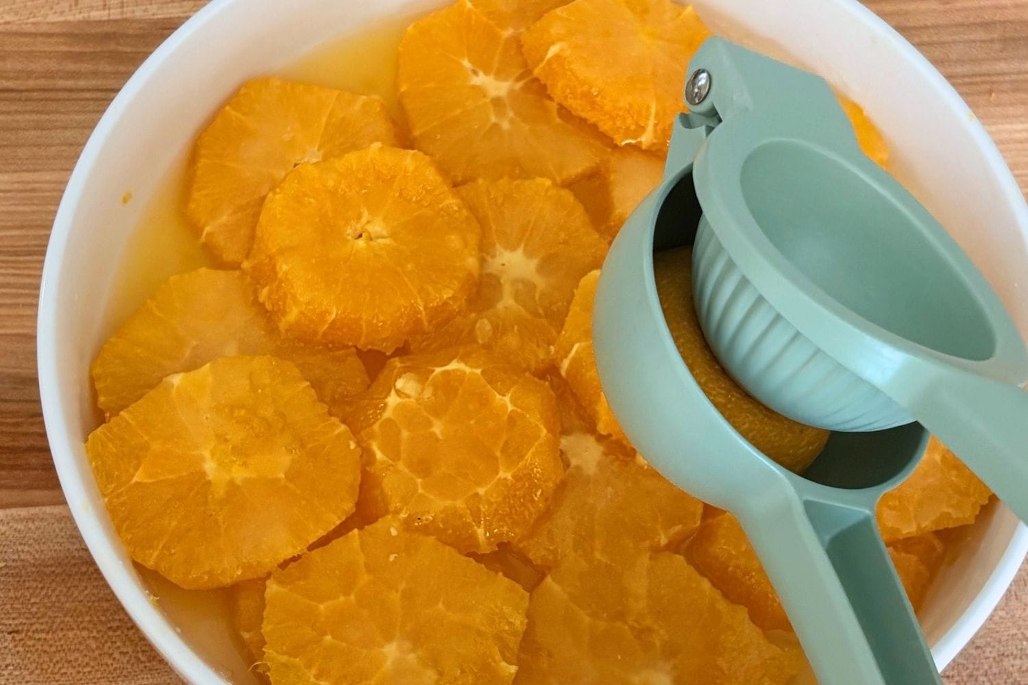 Fresh orange slices in a white bowl with a handheld citrus press squeezing lemon juice over the fruit.