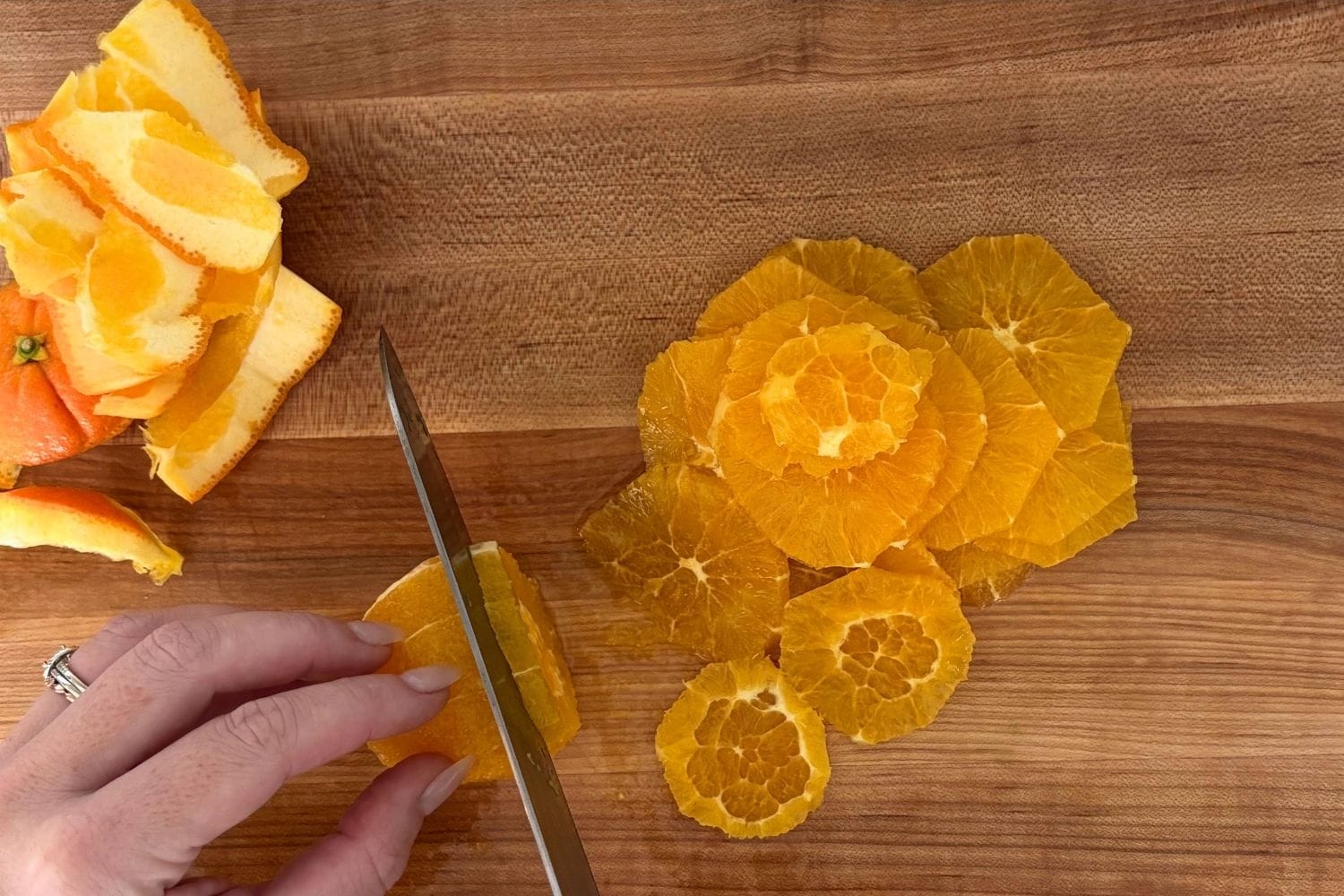 Peeled orange being sliced into thin rounds on a wooden cutting board for orange and cucumber salad.