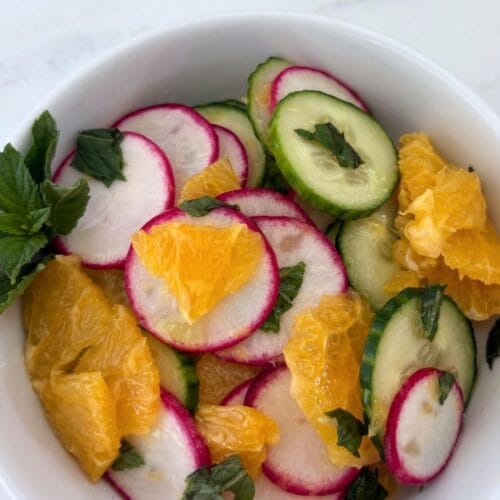 Orange and cucumber salad with thinly sliced radishes, English cucumber, fresh orange, and mint in a white bowl.