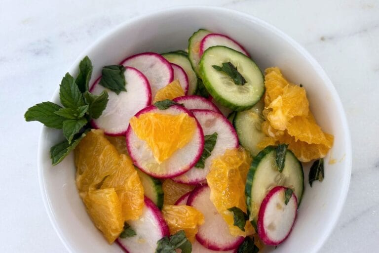 Orange and cucumber salad with thinly sliced radishes, English cucumber, fresh orange, and mint in a white bowl.