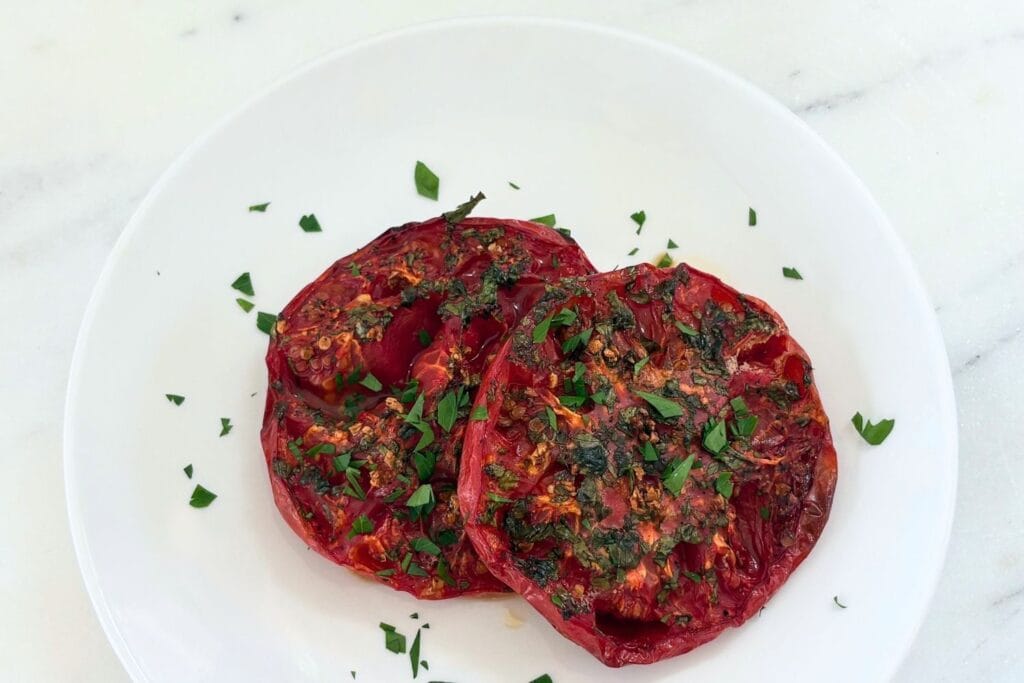 Marcella Hazan’s oven-browned tomatoes with garlic and parsley served on a white plate.