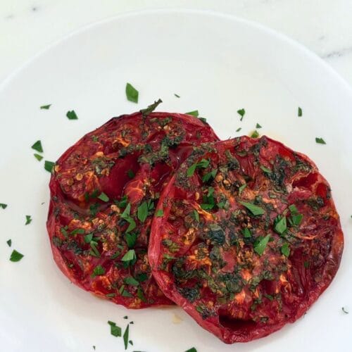Marcella Hazan’s oven-browned tomatoes with garlic and parsley served on a white plate.