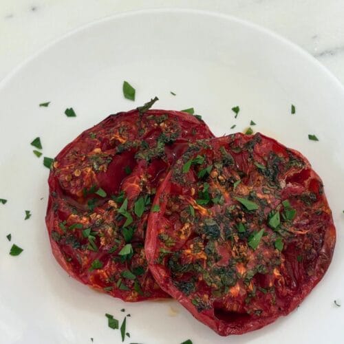 Marcella Hazan’s oven-browned tomatoes with garlic and parsley served on a white plate.