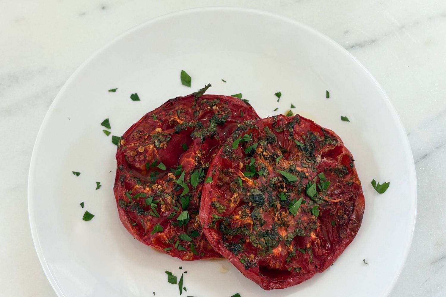 Marcella Hazan’s oven-browned tomatoes with garlic and parsley served on a white plate.