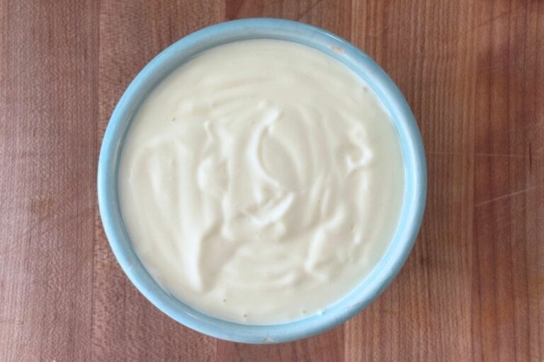 Overhead view of homemade mayonnaise in a small blue bowl on a wooden board.
