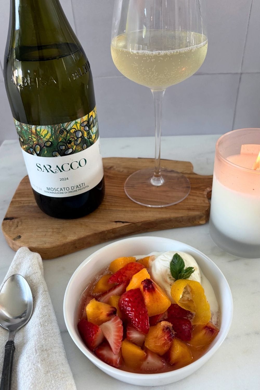 Bowl of peaches and strawberries in sweet white wine served with vanilla ice cream, mint, and lemon peel, alongside Moscato d’Asti.