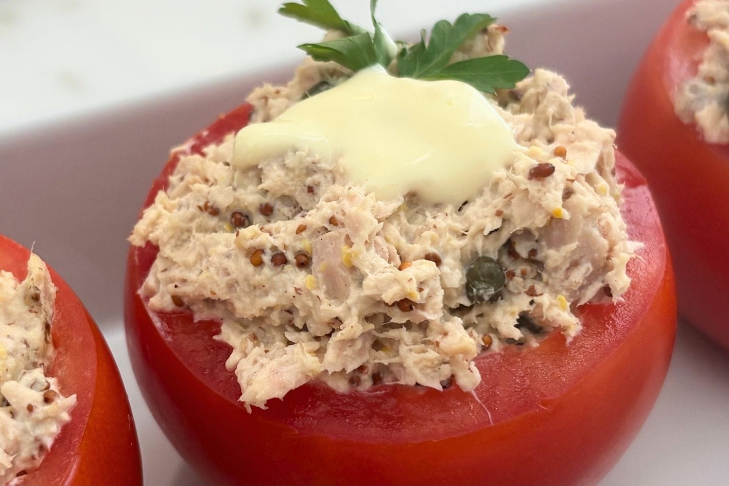 Close-up of a tomato stuffed with creamy tuna, capers, mustard, and mayonnaise, finished with homemade mayonnaise and parsley.
