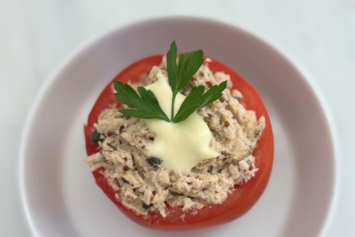 Tomato filled with creamy tuna, capers, mustard, and homemade mayonnaise, topped with parsley.
